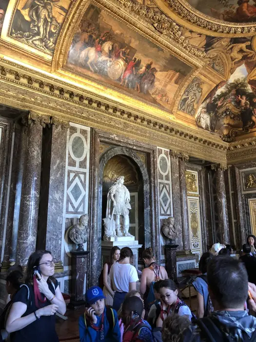 A statue of the King among the marble and gilt of the Grand Apartment — Versailles.