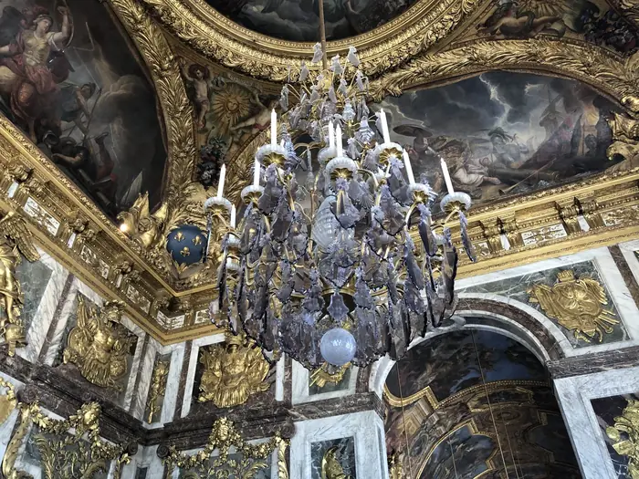 A great chandelier in the Hall of Mirrors, the painted ceiling ablaze behind it.