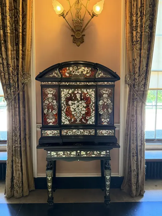 A cabinet inlaid with mother-of-pearl and pietra dura, between the curtains.